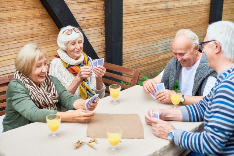 Vier aeltere Menschen spielen Karten auf einer Terrasse
