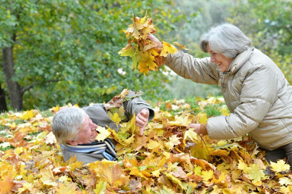 Aelteres Paar spielt lachend im bunten Herbstlaub