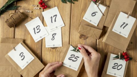 Selbst gemachter Adventskalender aus Papiertüten mit großen Zahlenkarten, eine Hand befestigt eine Karte