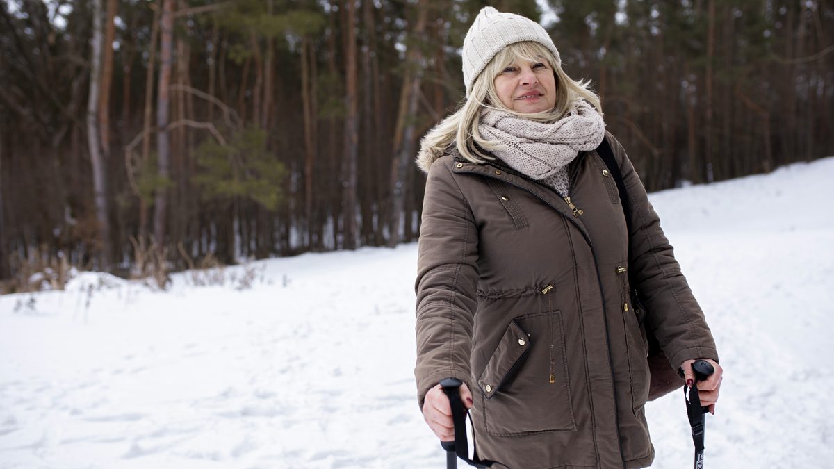 Aeltere Frau mit Muetze, Schal und Walking-Stoecken bei einem Winterspaziergang im Schnee