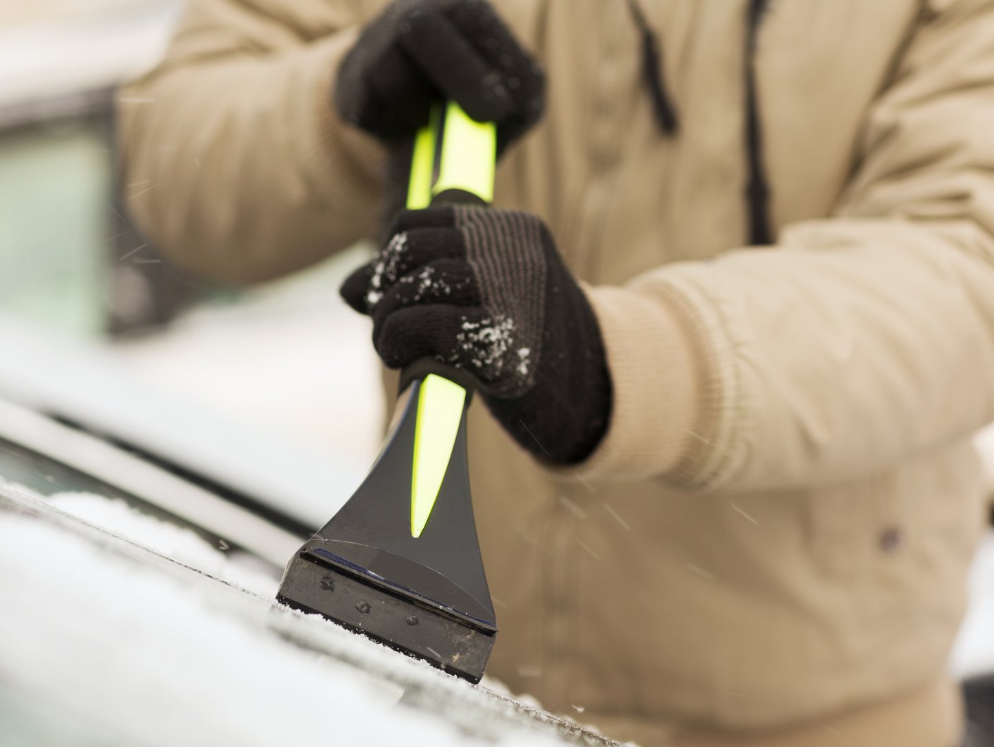 Hand im Winterhandschuh kratzt mit einem Eiskratzer mit langem Griff Eis von der Windschutzscheibe