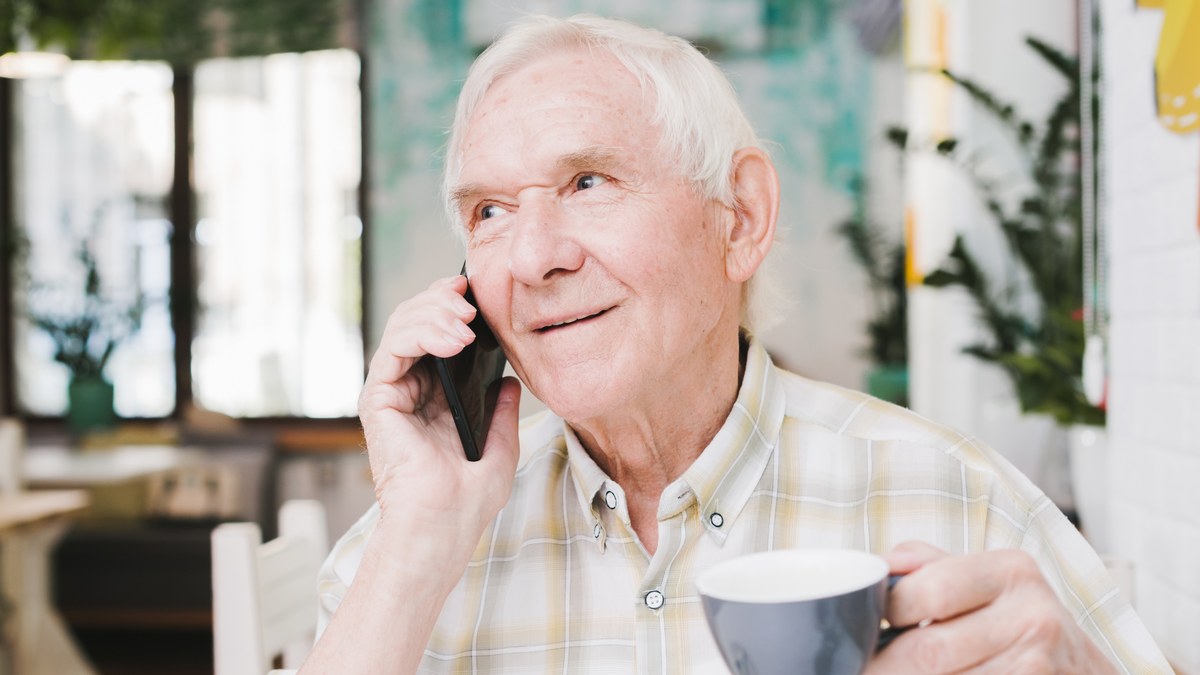 Aelterer Mann telefoniert mit dem Handy und haelt eine Kaffeetasse