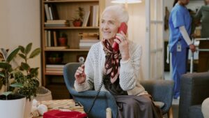 Aeltere Frau sitzt im Sessel und telefoniert laechelnd mit einem roten Festnetztelefon