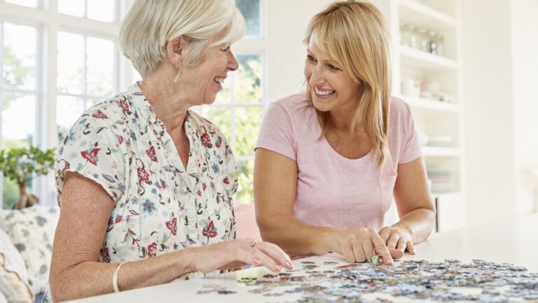 Eine aeltere und eine juengere Frau legen gemeinsam ein Puzzle an einem hellen Tisch