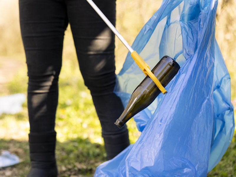 Greifzange hebt eine Flasche vom Boden auf