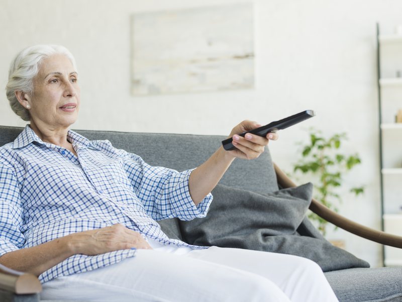 Aeltere Frau bedient auf dem Sofa den Fernseher