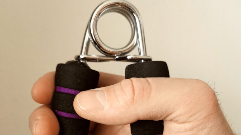 Hand drueckt einen Handtrainer mit Federbuegel und weichen schwarzen Schaumstoffgriffen