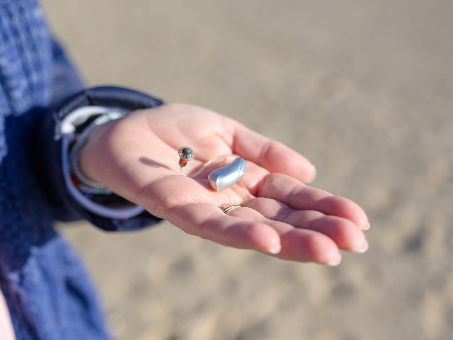 Offene Hand haelt ein Hinter-dem-Ohr-Hoergeraet und eine kleine Knopfzellen-Batterie
