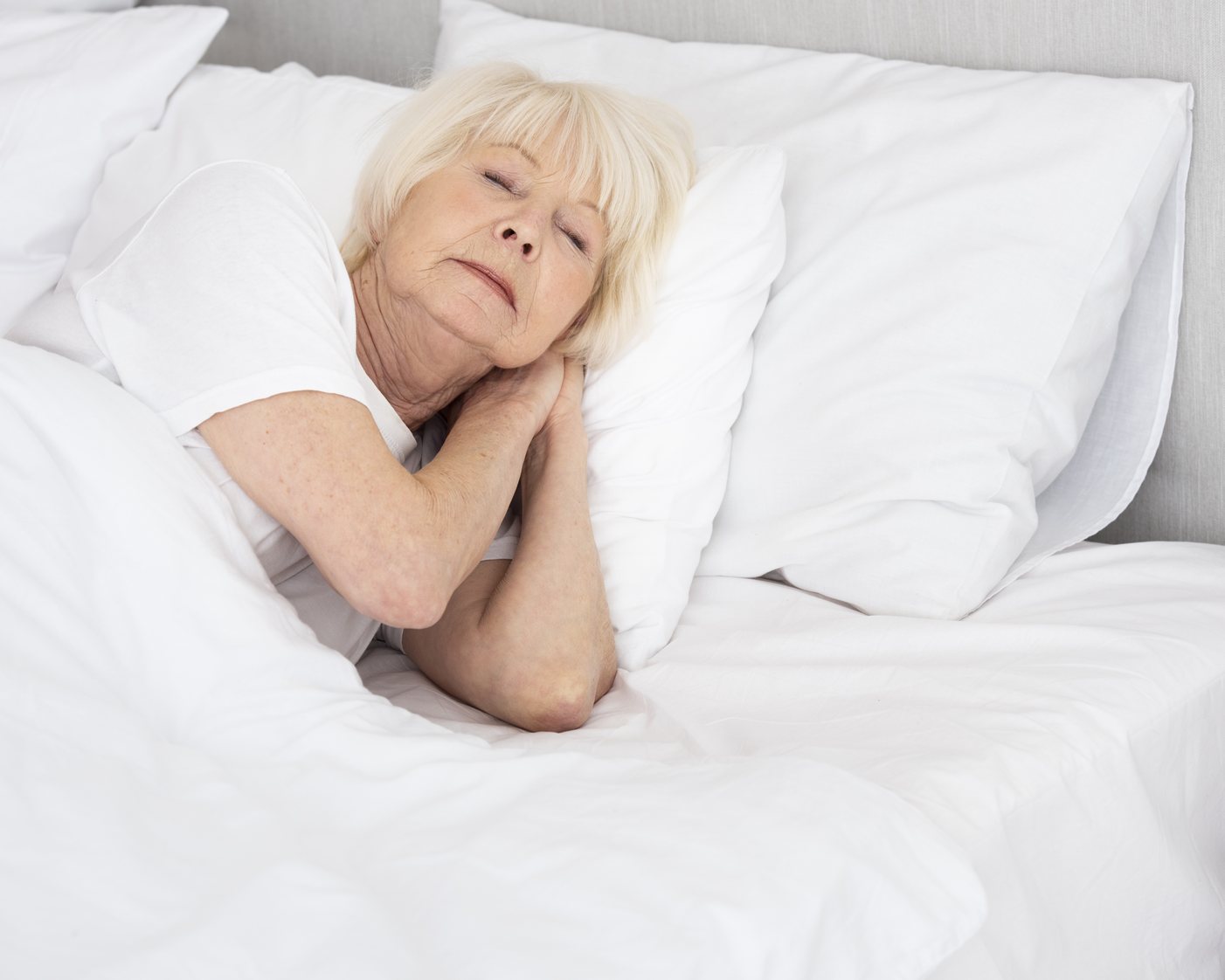 Aeltere Frau schlaeft ruhig auf einem weissen Kopfkissen in einem hellen Bett