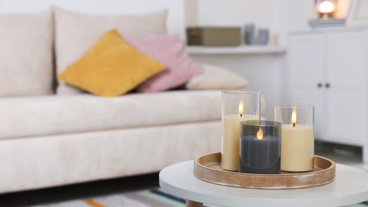 Drei LED-Kerzen in Glaszylindern auf einem Holztablett, auf einem kleinen Tisch vor einem hellen Sofa