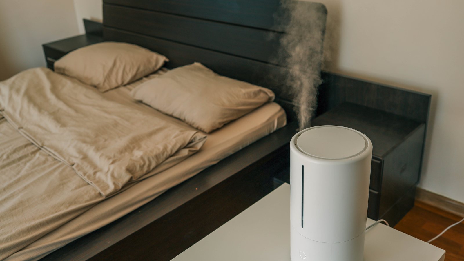 Weisser Luftbefeuchter steht auf einem Tisch neben dem Bett, feiner Nebel steigt auf