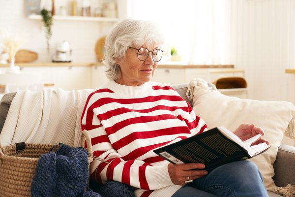 Ältere Frau mit Brille liest auf dem Sofa in einem Buch