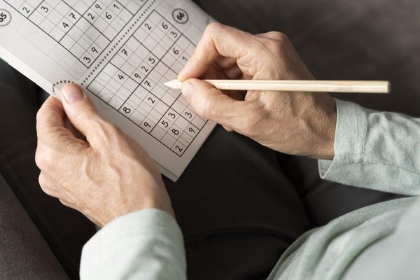 Ältere Hände lösen mit einem Bleistift ein Sudoku im Rätselheft