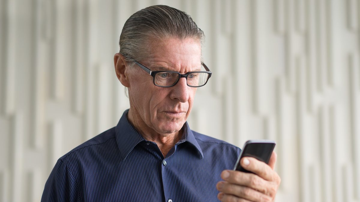 Aelterer Mann mit Brille liest skeptisch eine Nachricht auf seinem Smartphone