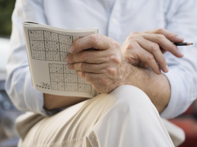 Aelterer Mann mit Sudoku-Raetselheft und Bleistift