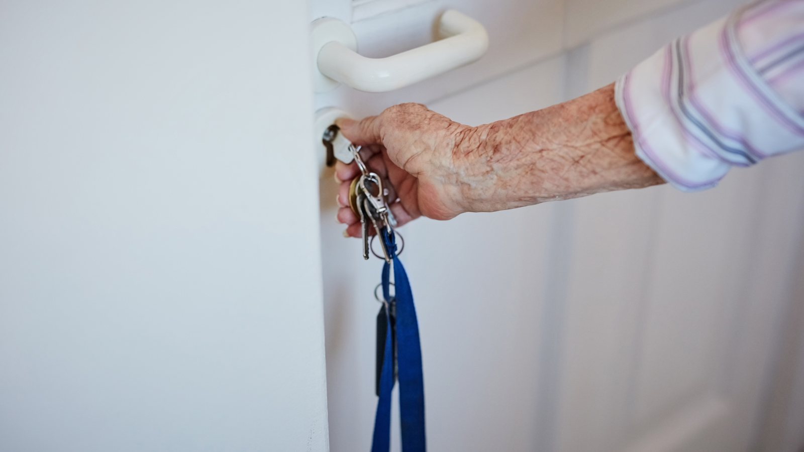 Aeltere Hand steckt einen Schluessel mit blauem Band ins Tuerschloss