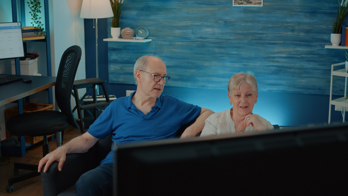 Aelteres Ehepaar sitzt auf dem Sofa und schaut fern
