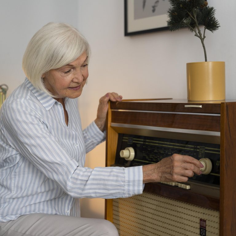 Aeltere Frau stellt an einem alten Radio im Wohnzimmer einen Sender ein