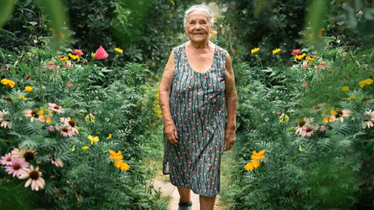 Aeltere Frau geht durch ihren bluehenden Garten