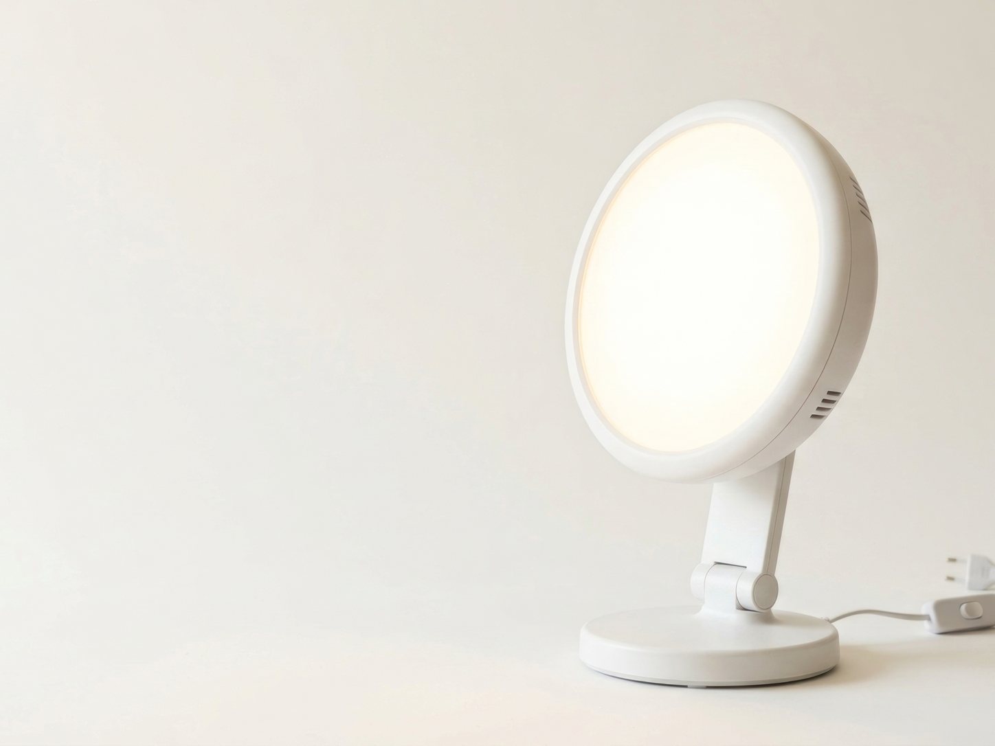 Runde weisse Tageslichtlampe mit hellem Leuchtfeld steht auf einem Tisch