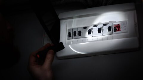 Hand leuchtet bei Stromausfall mit einer Taschenlampe in einen Sicherungskasten