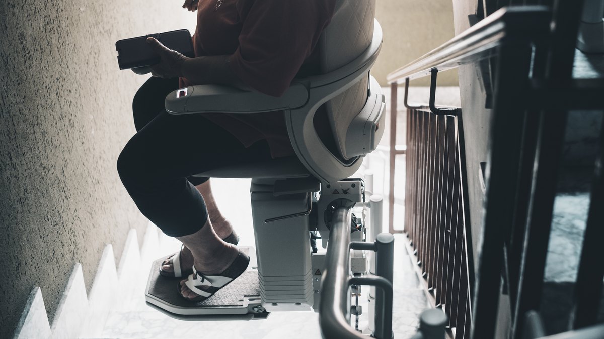 Person sitzt auf einem Sitzlift an einer Treppe im Haus