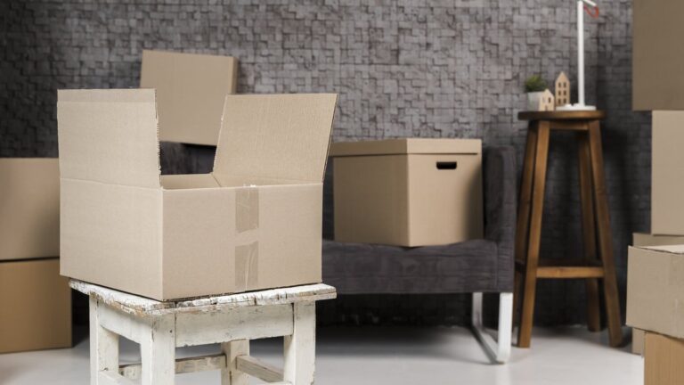 Leere Umzugskartons auf einem Holzhocker in einem halb ausgeräumten Wohnzimmer