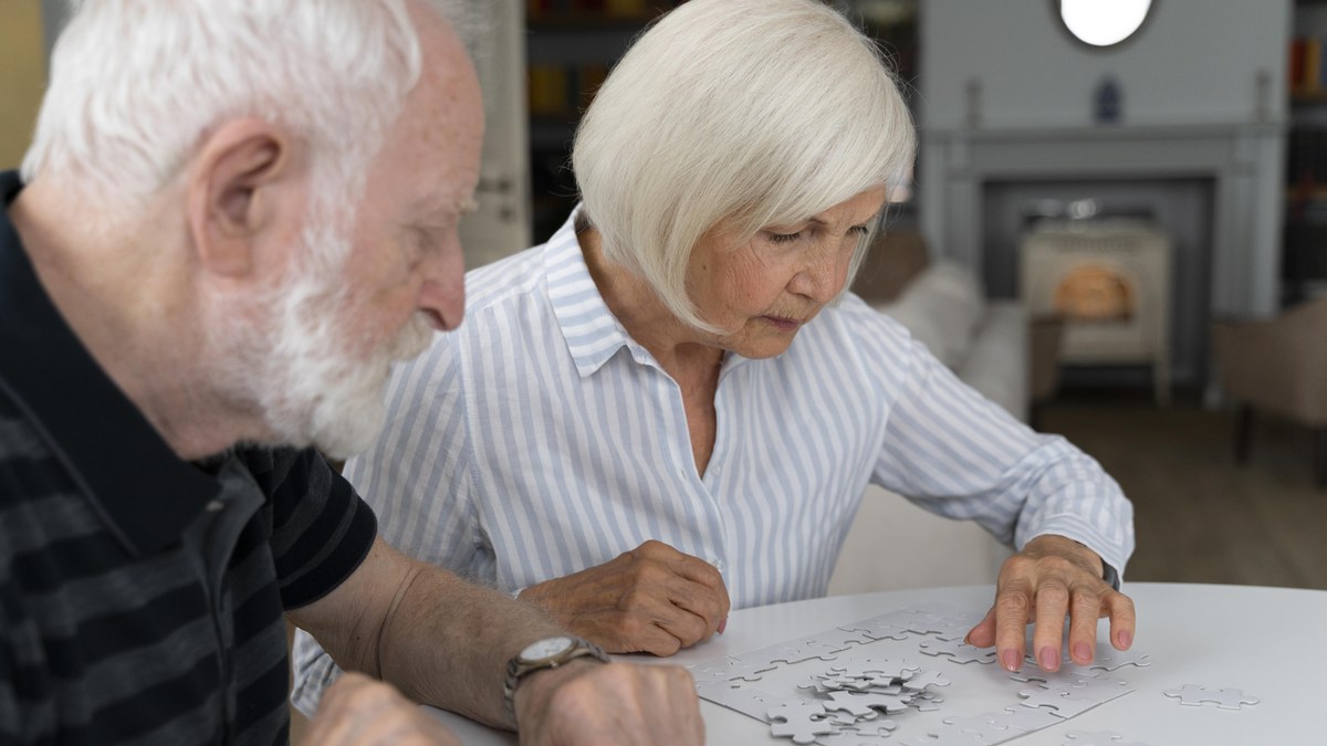Aelteres Paar sitzt am Tisch und legt gemeinsam ein weisses Puzzle