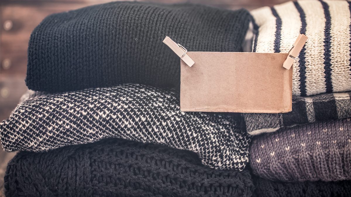Gestapelte Strickpullover mit einem leeren Pappschild an zwei Waescheklammern